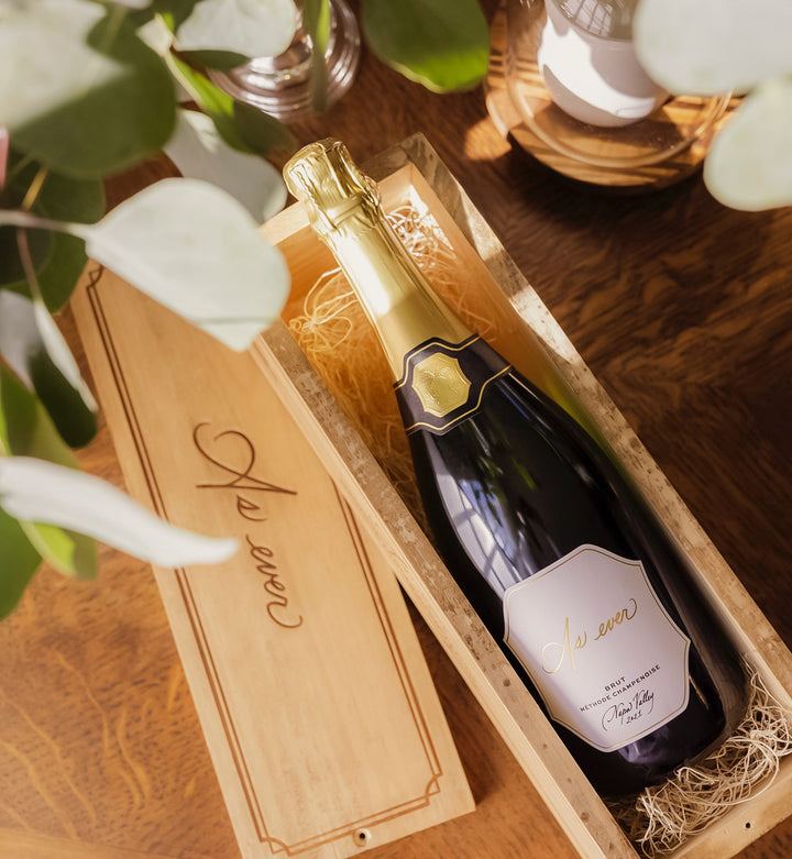 Bottle of As ever Brut in an As ever wooden crate with decorative elements on a wooden surface
