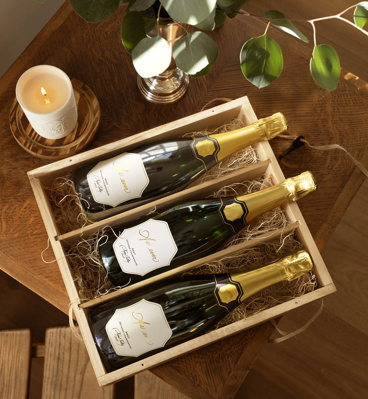 Three bottles of As ever wine in an As ever wooden gift crate on a wooden table with a candle and plant